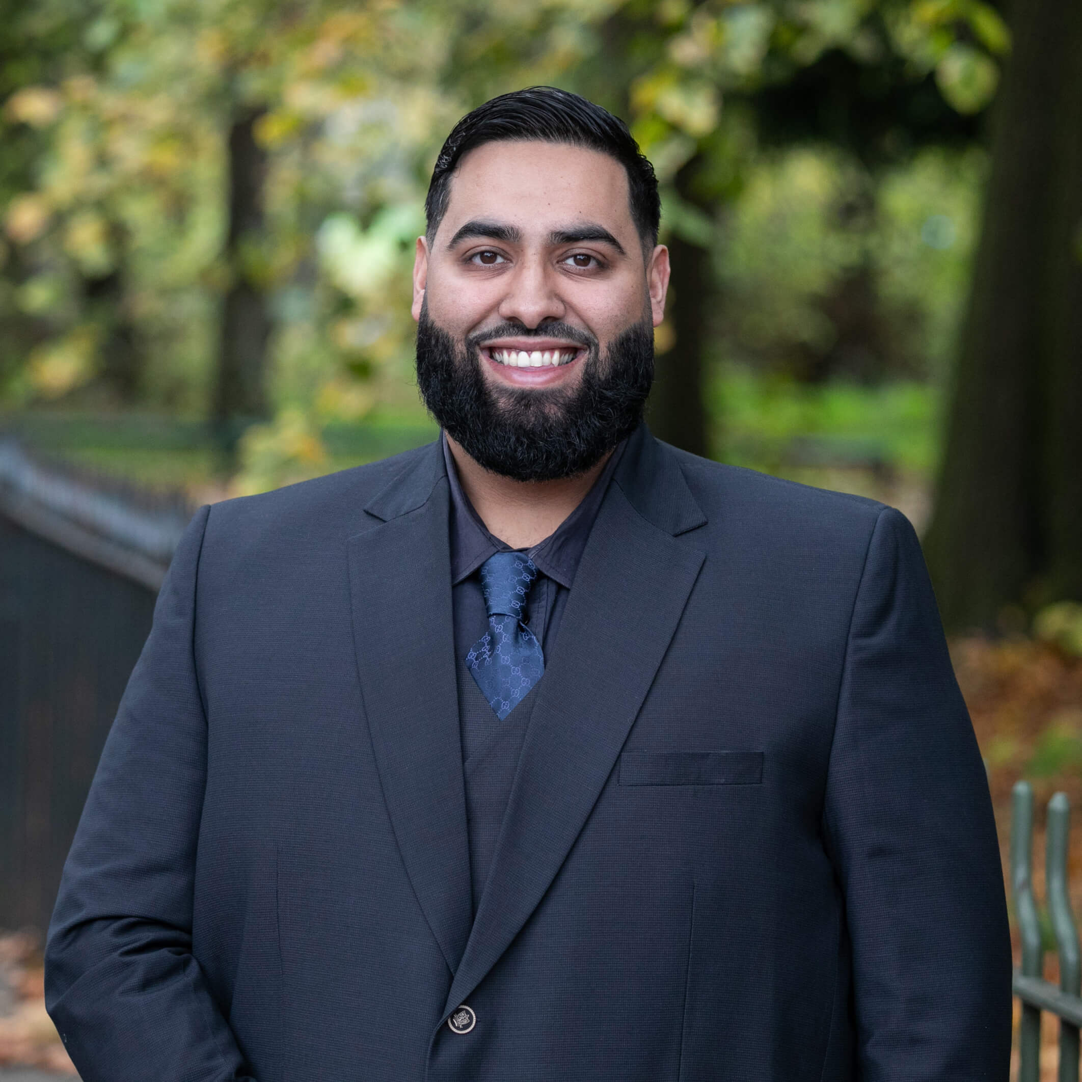 Ali Shah, a smartly-dressed solicitor, standing in a vibrant park.